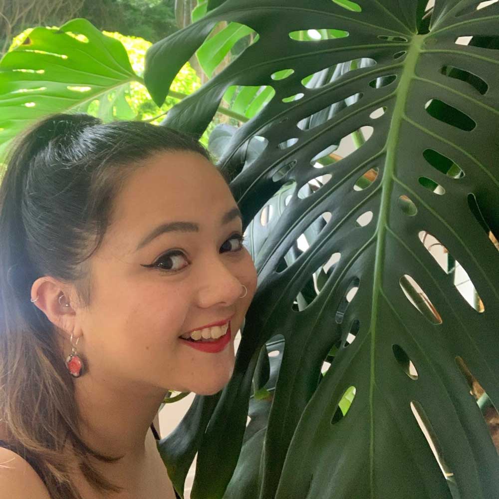 Jasmine Yahkup, surface pattern designer, stands next to a towering Monstera plant, showcasing her botanical inspiration.